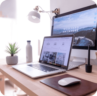 table with office supplies like a laptop in front of a screen, a plant, a mousepad with mouse